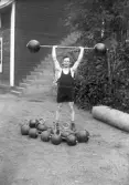Kraftkarl ifrån atletklubben Heros poserar lyftandes en viktstång med klotvikter, tidigt 1900-tal.