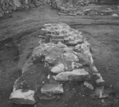 Gudsberga kloster, Husby socken. Pelarbas i kyrkans mitt mot den norra mren. Pelaren är uppmurad i tegel med en klack av gråsten som sträcker sig västerut.