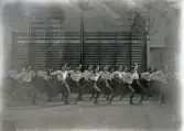 En grupp kvinnliga gymnaster i blus och s.k. ballongbyxor, har gymnastik i gymnastiksalen på dåv. Seminariet.