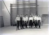 En mindre skolklass, uppställda i en gymnastiksal, klädda för gymnastik.