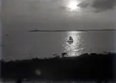 Landskap med hav och en segelbåt i motljus. I bakgrunden syns en fyr.
