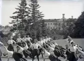 En trupp kvinnliga gymnaster övar i det fria utanför dåv. seminariet, dvs numera Ringsbergsskolan i Växjö.  I bakgrunden syns skolans växthus och dåv. cellfängelset.