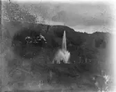 Mörkt foto av en park med en stor fontän. I bakgrunden skymtar trol. en restaurang.