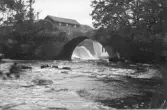 Bobergs Kvarn vid Suseån, Heberg. Vy söderifrån mot stenvalvsbron mot forsen och kvarnbyggnaderna på andra sidan vägen.
