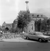 Parkering av cyklar och bilar med Örebro slott i bakgrunden, 1970-tal