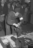 Hantverkstävling på Rotundan den 2 april 1950. En smidesarbetande man alternativt en sotare vid ett arbetsbord.