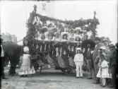 En praktfullt dekorerad vagn, fylld med (mestadels) flickor i stora hattar, inför den stora Barnens Dag-paraden.