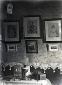 Interiörfoto från en salong. Man ser en soffa med s.k. antimakasser på ryggstödet, en finare fotogenlampa 
och en mängd tavlor (fotografier) på väggen.