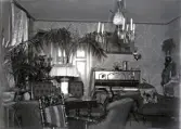 Interiör från en salong. I bakgrunden syns ett piano m.m. och i förgrunden en sittgrupp med en soffa, några stolar, en fåtölj m.m. 
I taket hänger en stor taklampa för fotogen och levande ljus.

Kan möjl. vara en interiör från Dansjö gård, Lekaryds sn., som innehades av
fotografens kusin, godsägare Edvard Danckwardt (1856-1923).