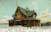Handkolorerat vykort daterat 28 augusti 1907 med Särö järnvägsstation i trä som motiv. Vykortet är poststämplat 1907-08-30.