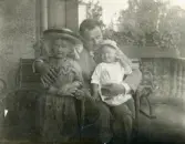 Foto av två barn i fars famn (enligt text skriven i albumet).