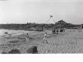 Vy över badstranden i Fjärde vik på Getterön. Uppe på berget ligger en restaurang  (Sunds?) med flaggspel från flaggstången.