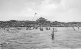 Badliv i 4:e vik på Getterön. Vy över vattnet med badande mot berget där Sundhs restaurang ligger med stor uteservering. 1920-talet.