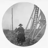 Britta Kronvall står med sin cykel bredvid en träkonstruktion med stege, möjligen en klockstapel.