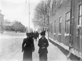 Två kvinnor (familjen Danckwardt ?) går längs en gata, någonstans i Växjö, en kall vinterdag. I bakgrunden skymtar några tonårspojkar i realskolemössor m.m.