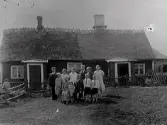 Otto och Ida i Bäckarp med en del familjemedlemmar framför sitt hus. I mitten sonen Sven med Berta i Hult, Gunnarp. Huset har två ingångar och den högra delen av taket ser mer nylagt ut. Av skorstenen att döma har taktäckningen tidigare varit tjockare.