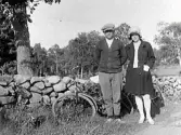 Syskonen Karl Persson och Sigrid Persson i Kila, Åbacken i Gällared socken. De är på cykeltur och har lagt cyklarna mot stengärdsgården för fotograferingen i solen.