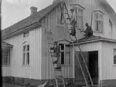 Nybyggda huset i Tornared målas. Färgen var vit med gröna fönster och vindskivor. På stegen överst står Karl Johansson, Haxered, nedanför Adolf Svensson. På taket sitter John Johansson hukad, som verkar ha lånat ut sin kamera för tillfället. Adolf var Johns morbror som tog över gården 1915. Adolfs mor Anna Beata Persdotter levde och bodde kvar till 1922.