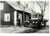 Bil med flak, en T-ford, på gårdsplanen invid bostadshuset på Klevs gård i Askome 1925 samt pojke med cykel.