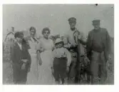 Kvinnor, män och ett par pojkar fotograferade på en äng utanför huset, Lorensberg, Varberg ca 1925.  Fr v: gossen Sjöberg, Sofia Bengtsson, okänd, gossen Sjöberg (?), Birger Johansson som bryner en lie och Otto Bengtsson