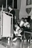 Ordföranden i svenska Unicef-kommittén Lisbeth Palme i talarstolen vid en sammankomst för Unicef i Fässbergsgymnasiets aula i Mölndal, slutet av 1980-talet eller början av 1990-talet.