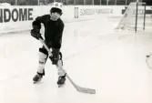 En ung ishockeyspelare på ishockeyskolan. Fotografiet är taget vid Mölndals konstisbana vid Ågatan i Trädgården, Mölndal, ca 1970-1976.