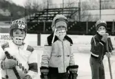 Tre unga ishockeyspelare på ishockeyskolan. Fotografiet är taget vid Mölndals konstisbana vid Ågatan i Trädgården, Mölndal, ca 1970-1976.