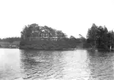 Byggnad på andra sidan vattnet, bakom träden, eventuellt ett kapell.