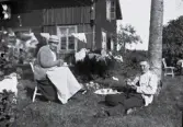 Dam och man sitter i en trädgård och fikar, tidigt 1900-tal.