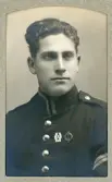 En ung man i uniform (korpral) med förtjänstmärken. 
Bröstbild, halvprofil. Ateljéfoto.