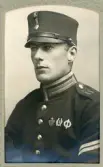 En ung man i uniform (m/95, korpral) med kepi och förtjänstmärken.
Bröstbild, halvprofil. Ateljéfoto.