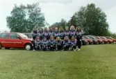 Lagbild av fotbollslaget Jitex BK på Krokslättsvallen i Mölndal, juli 1991. I bakgrunden sponsorbilar från Ford Motorverken.