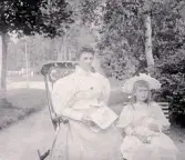 Foto av en kvinna och en flicka som sitter i en trädgård. Bildtext i album: 