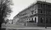 Sparbanksfastigheten på Kungsgatan, kv. Sunaman, under uppförande, med en vy utmed Kungsgatan med järnvägsstationen i fonden, bakom vilken läroverket tornar upp sig.