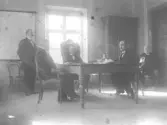 På rådhuset vid torget höll magistraten sammanträde. Borgmästaren Bengtse´n i stolen med ryggen åt fönstret, länsman Ankarloo t.v. om honom. Rådman Svensson till höger rådman Tomander vid fönstret C.P. Pettersson, rådman vid dörren. (A.S.)