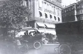 Fotot visar en gatuscen från Paris med en tidig bil och en hästdragen vagn framför en byggnad med texten 