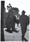 Foto av några, troligen präster med prästkappor och hattar, på promenad till vänster i bild, 1921.