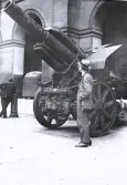 Foto av tandläkare Gunnar Högberg ståendes bredvid en stor kanon, troligen ett artilleripjäs, troligen på Musée de lÁrmée i Paris, 1921.