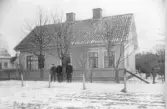 Bostadshuset uppfört 1885 av kustroddare Johan Bert Johansson. Till vänster ses västra bostadshuset på tomt nr 3 och gaveln på ett bostadshus på tomt nr 5, båda i samma kv.  Personer fr. h. Tulluppsyningsmannen J A Johansson, son till kustroddaren, hustrun A C Johansson, f. Ljungblad, och sonen N G A Johansson.  Byggnaden revs 1983.  Fotot skänkt av Britt Marie Vennersten Varberg, sonsondotter till J B Johansson.
