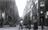 Foto av ett kvarter i, troligen Amsterdam, med människor i rörelse, 1924-25.