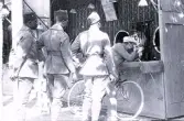 Foto av några män i uniform som väntar på sin tur att få skjuta ner saker i ett tivoli-stånd samt en man med cykel som prövar sin lycka någonstans på franska atlantkusten, 1924-25.