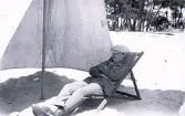 Foto av tandläkare Gunnar Högberg sittande i en strandstol under ett parasoll någonstans på franska atlantkusten, 1924-25.