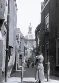 Foto av en gränd med en kvinna längst fram i bild och där man i bakgrunden kan se kyrkan Marekerk i Leiden , Nederländerna, 1924-25.