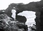 Foto av en kvinna som står vid en klippformation vid vattnet, troligen någonstans på franska atlantkusten, 1924-25.