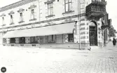 Uppfört av Falkenbergs Sparbank 1895-1896. Indragen butiksentré jämte trappa 1957.(försl. t. bev. pl.)  På bilden finns J E Eliassons AB Manufaktur inrymt i affärslokalen.