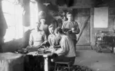 Träskokängor spikas 1920 hos Hjalmar Svenssons - interiör, 5 män är samlade vid skomakaretavlan. Troligen skomakaren Karl Börjesson t.v. vid fönstret bakom honom lärpojken (med mössa) därjämte tre gesäller.