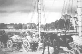 Lastning av kantsten. Personer fr.v. på kärran Erik Jakobsson , född 1904 i Halmstad,. Arbetaren (okänt namn) i keps arbetade troligen vid kajen som stenlastare anställd av Bolaget. Mannen i hatt Karl Skantz, bolagets förman vid upplagsplatsen här vid Dragvägen. Kantstenen kom troligen från Stenhuggeriet i Halmstad. Vagnar och hästar tillhörde Bolaget dvs det stenbolag som behärskade stenexporten från Halmstad. Den tvåmastade skutan är förmodligen tysk. Annars ägde Bolaget två skutor för stenfrakt - Vind och Dora, de var enmastade.