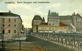 Östra Storgatan i Jönköping vid hamnkanalen. Till vänster om bron ligger Bankaktiebolaget Södra Sverige och i huset till höger Konfektions AB Norden och Cigarr och Tobakshandel. Vykort skrivet 1911-06-28.