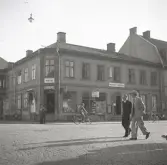 Korsningen Storgatan/Klostergatan (kv. Stormen) med bl a Lundbergs affär på hörnet, följt av Foto-Centralen och ingången till Vigfors matsalar.
Två herrar i kostym och hatt passerar.