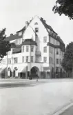 Ett reveterat flerfamiljshus i nationalromantisk stil med burspråk m.m. i ett gathörn. 
Hörnet Rådmansgatan/Skolallén, Landskrona. (Rådmansgatan 15-17).